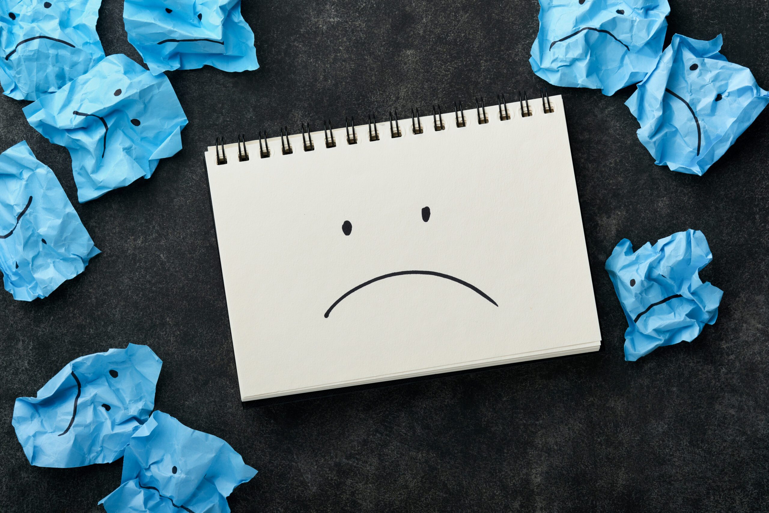 Blue crumpled sticky notes blank with drawing sad face on black background with copy space ready for your message. Blue Monday and mental health concept idea. Flat lay copy space on black background.